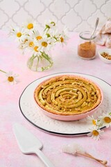 Tart on a sand dough with rhubarb and walnuts laid out in a circle in pink for baking on a pink concrete background. Recipes for rhubarb.