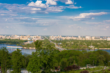 Fototapeta premium A stunning panoramic shot of Kyiv showcasing the Dnipro River, scenic greenery, and bustling urban architecture beneath a vibrant blue sky.