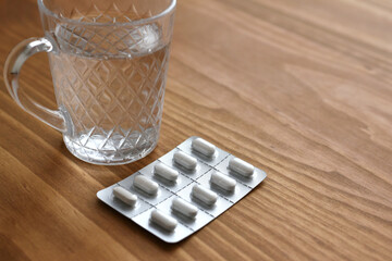 Close up of a glass of water and medicine tablets in blister pack on wooden background