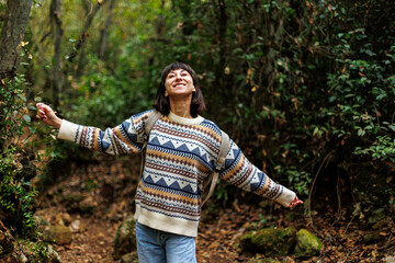 girl in a stylish sweater and with a backpack enjoys a walk in the forest. trekking in the forest. a girl with a backpack walks in the forest. trekking and hiking.