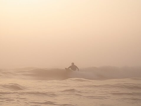 Surfer silhouetted against a hazy sunrise, riding a wave in the ocean. - Powered by Adobe