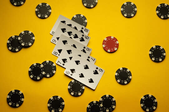 Poker cards with a rare straight flush combination lie on a yellow table with chips. The concept of a successful win after gambling in a poker club