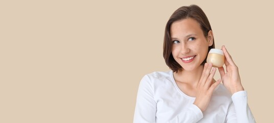 Young woman with acne problem holding jar of cream on beige background with space for text