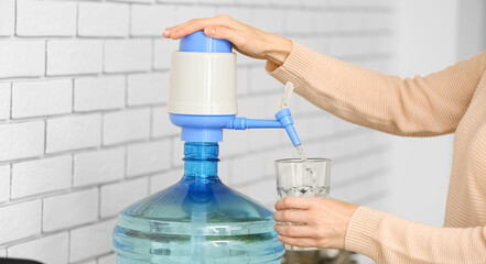 Woman pouring clean water from bottle into glass in kitchen, closeup