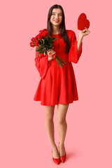 Beautiful young woman with kiss marks on her face holding bouquet of roses and red paper heart on pink background