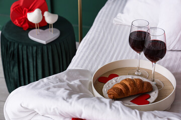Tray with glasses of wine and croissant on bed, closeup. Valentine's Day celebration
