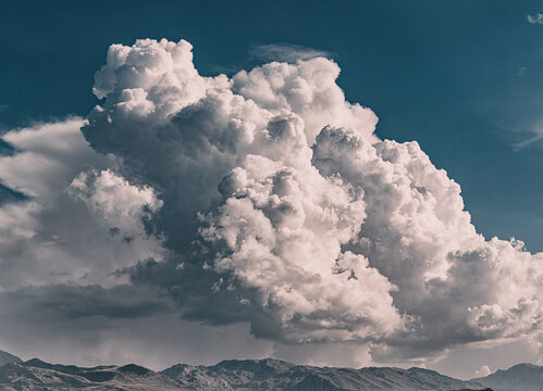 Dramatic cumulonimbus cloud forming above a mountain range, creating a stunning contrast between the bright white clouds and the dark blue sky