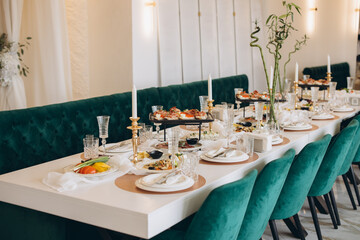 Elegant white wedding table setting with green velvet chairs and golden candlesticks