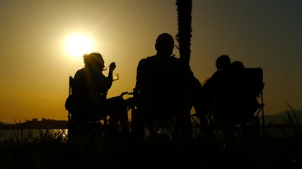 Family enjoying sunset conversation. Vibrant sunset casts silhouettes of a family sharing a peaceful moment by the lake, engaging in heartfelt conversation and enjoying the tranquility of the evening