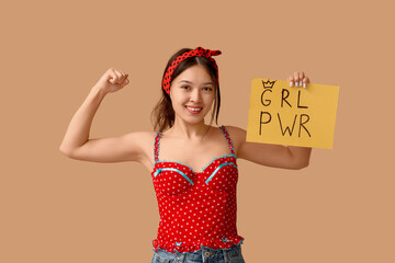 Beautiful young Asian pin-up woman holding card with text GIRL POWER and showing her muscles on...