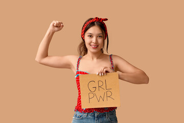 Beautiful young Asian pin-up woman holding card with text GIRL POWER and showing her muscles on...