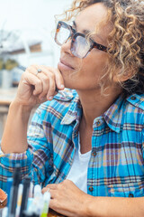 Daydreamer people concept. Woman sitting indoors wearing glasses while painting on a canvas,...