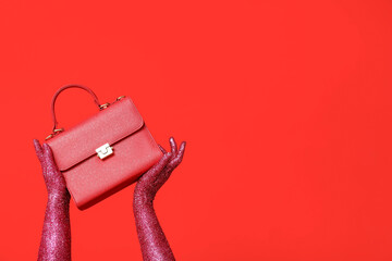 Female hands covered with glitter and stylish handbag on red background
