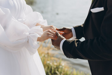 Groom Placing Wedding Ring on Bride's Finger During Interracial Wedding Ceremony