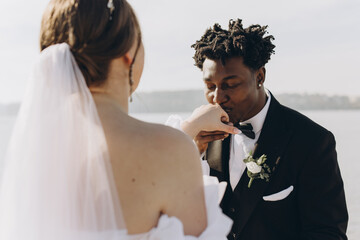 Groom kissing bride's hand during interracial wedding ceremony