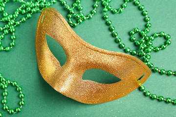 Shiny golden carnival mask with beads for Mardi Gras celebration on green background
