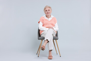 Fototapeta premium Senior woman on chair against light background