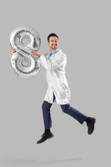 Male doctor with balloon in shape of figure 8 jumping on grey background. International Women's Day