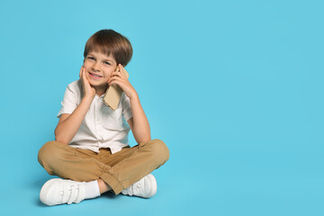 Cute little boy talking on smartphone against light blue background, space for text