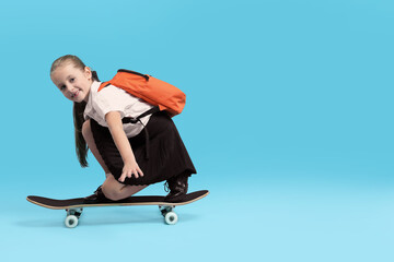 Little girl standing on skateboard against light blue background, space for text