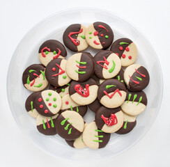 Chocolate-dipped, shortbread cookies with red and green decorations in round container.