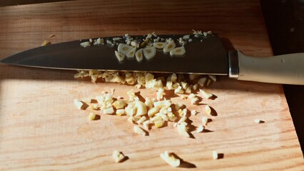 Knife and freshly chopped garlic on a wooden cutting board in sunlight