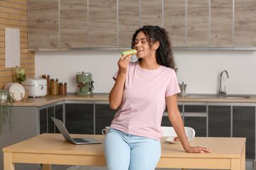 African-American woman eating tasty eclair in kitchen