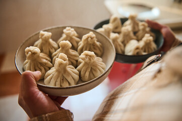 Hand holding plates of homemade Georgian dumplings in a kitchen setting