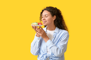 African-American woman with tasty eclairs on yellow background