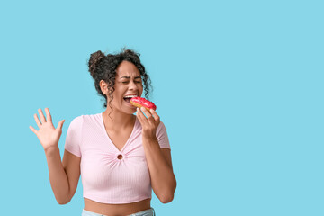 African-American woman eating tasty eclair on blue background