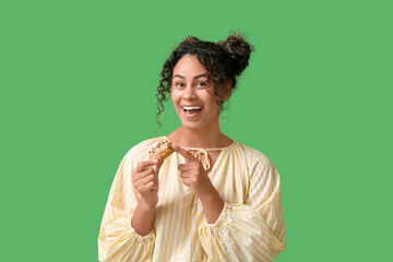 African-American woman eating tasty eclair on green background