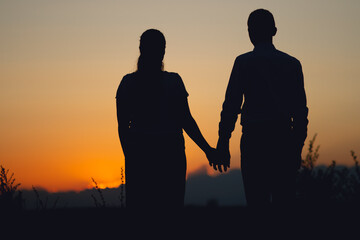 Silhouette of a couple in love walking together at sunset in summer. Romantic scene of lovers.