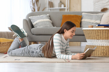 Beautiful young happy woman reading book lying on floor at home