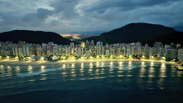 Imagem a&eacute;rea noturna de praia Pitangueiras no Guaruj&aacute; com muitas nuvens de chuva e diversos pr&eacute;dios residenciais usados para loca&ccedil;&atilde;o para temporada.