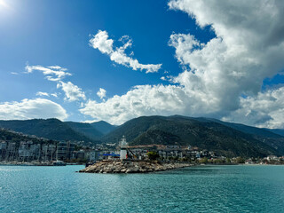 Lighthouse on rocky island near coastal town under bright blue sky with clouds