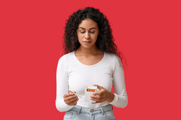Concerned young African-American woman with pack of cigarettes on red background. Stop smoking...