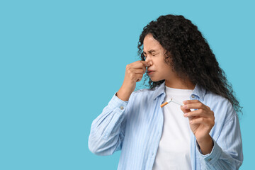 Disgusted young African-American woman with broken cigarette on blue background. Stop smoking...