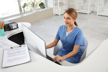 Female medical intern working with computer at reception in clinic