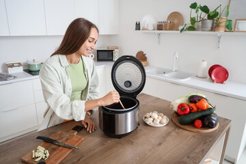 Young woman with spoon stirring food in multi cooker at home