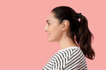 Young woman with hearing aid on  pink background