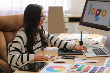 Young female graphic designer working with tablet and laptop at table in office