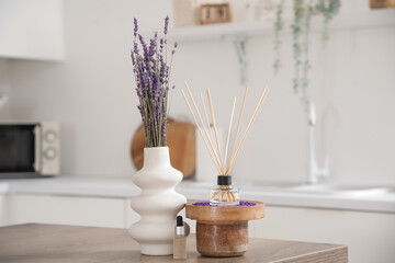 Reed diffuser, vase with lavender flowers and essential oil on table in kitchen, closeup © Pixel-Shot