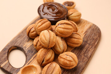 Wooden board of sweet walnut shaped cookies with boiled condensed milk on beige background, closeup