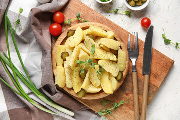 Wooden plate of tasty potato salad with pickled cucumber and tomatoes on white background