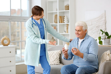 Obraz premium Female doctor and mature man with pills sitting on sofa at home