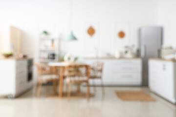 Blurred view of light kitchen with white counters, shelf unit and dining table