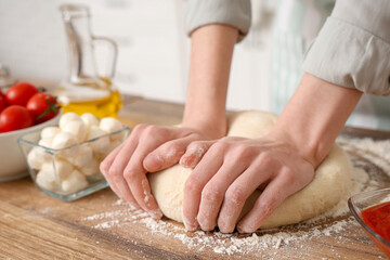 Woman kneading dough for pizza near table in kitchen