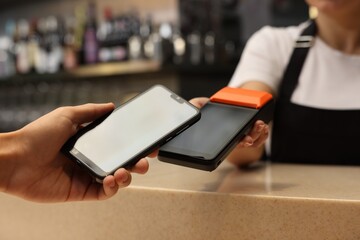 Man paying with smartphone via terminal in cafe, closeup