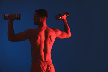 Man exercising with dumbbells in red light on blue background, back view