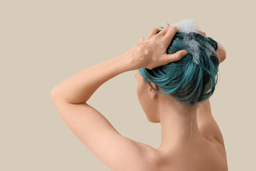 Young woman washing her blue hair on beige background, back view